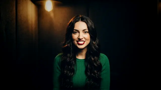 Tatum smiling in a dark booth under a single bulb